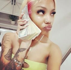 a woman with pink hair and tattoos holding money in front of her face while looking at the camera