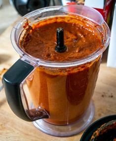 a blender filled with red sauce on top of a wooden table