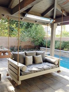 a porch swing with cushions on it in front of a swimming pool