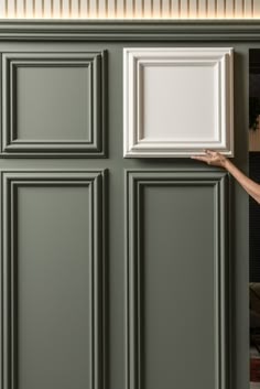 a woman is holding up a white frame in front of a green wall with vertical paneling