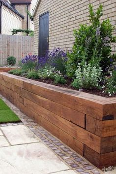 a wooden planter filled with lots of flowers next to a brick wall and grass