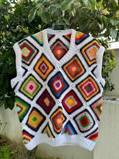 a crocheted sweater hanging on a clothes line next to a tree and bushes