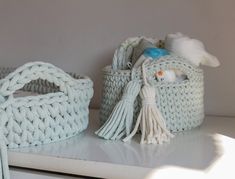 two knitted baskets sitting on top of a white shelf next to each other, one with a tassel hanging from it