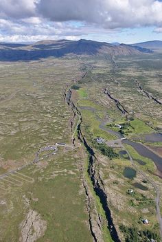 an aerial view of a river running through the middle of a green field with mountains in the background