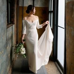 a woman in a white wedding dress is holding a bouquet and looking out the window