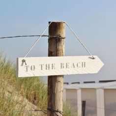 a sign that says to the beach hanging on a wooden post in front of some grass