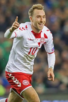 a male soccer player is running with the ball in his hand and smiling at the camera