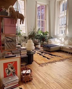 a living room filled with furniture and lots of windows next to a wooden floor covered in books