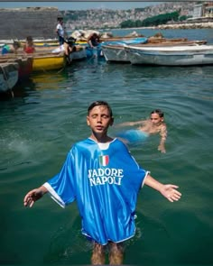 a young man standing in the water with his arms out and two other people swimming behind him