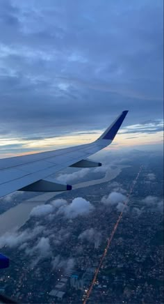 the wing of an airplane as it flies through the sky with clouds and buildings in the background