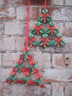 two origami christmas tree ornaments hanging on a brick wall