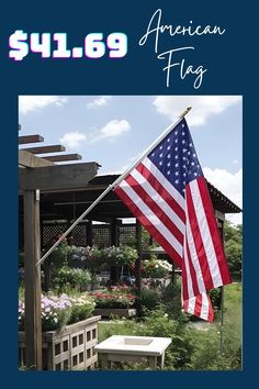 an american flag hanging from the side of a wooden pergolated structure with flowers in the background