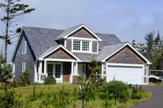 a house that is in the middle of some grass and trees with a driveway leading to it