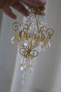 a hand is holding a gold and clear chandelier with crystal beads on it