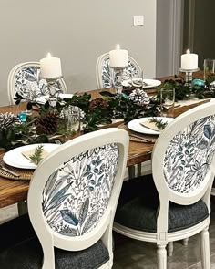 a dining room table set for christmas with candles and greenery on the table top