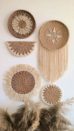 three woven baskets hanging on the wall with dried grass in front of them and plants