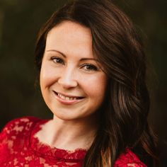 a woman in a red dress smiling at the camera with trees in the back ground