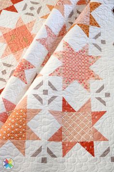 an orange and white quilt is laying on top of a tablecloth that has been made into a star pattern