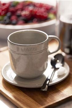 a cup and saucer sitting on top of a wooden cutting board next to a bowl of berries