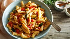 a bowl filled with pasta and vegetables on top of a wooden table next to spices