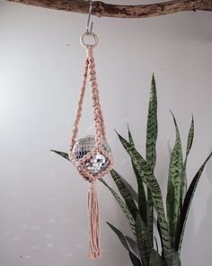 a pink macrame hanging from a wooden branch next to a potted plant