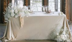 a table with white flowers and champagne glasses on it in front of a large window