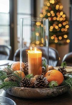 a candle is lit in a glass bowl with pine cones and oranges on the table