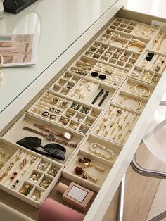 a drawer filled with lots of jewelry on top of a white counter next to a chair