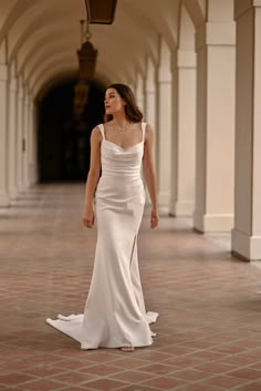 a woman in a long white dress is walking down the street with her hand on her hip