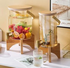 two glass vases with fruit in them sitting on a table next to each other