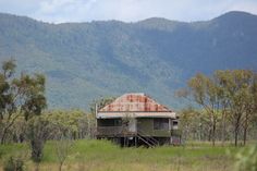 an old run down house in the middle of a field with mountains in the background