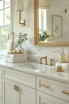 a white bathroom with gold accents and marble counter tops, along with towels stacked on top of the sink