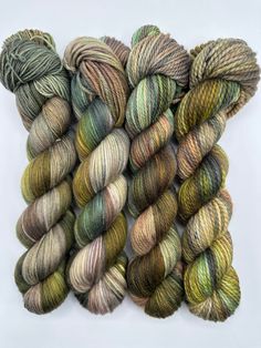 several skeins of yarn laid out on a white surface, one is green and the other is brown