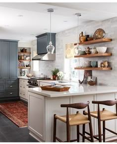 a kitchen with gray cabinets and white counter tops, two stools in front of the island