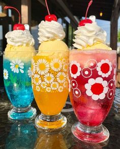 three different colored drinks sitting on top of a table next to each other with ice cream and cherries