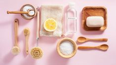 various wooden utensils and cleaning supplies on a pink surface with lemon slices, soap, scrubs, toothpaste, and other items