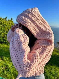 a woman wearing a pink crochet sweater looking out at the ocean with her hands on her face