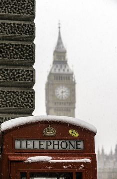 a red phone booth with big ben in the background during a snow storm, london