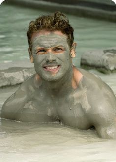 a man with mud on his face is in the water and smiles at the camera