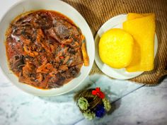 a white bowl filled with meat and sauce next to a lemon wedge on top of a table