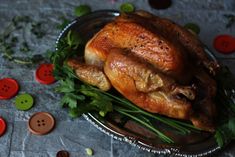 a roasted turkey on a platter with green leaves and red buttons around the edges