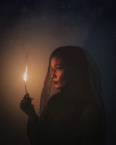 a woman holding a lit candle in her hand and looking up at the night sky