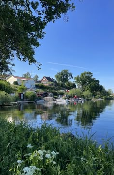 a lake with houses on the shore and trees in the foreground, surrounded by greenery