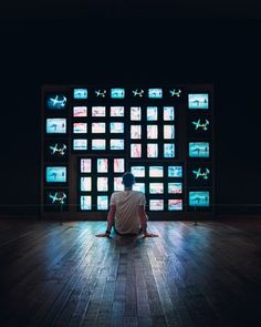 a person sitting on the floor in front of a wall with multiple televisions