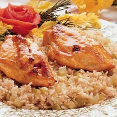 two pieces of chicken and rice on a plate with yellow flowers in the background, ready to be eaten