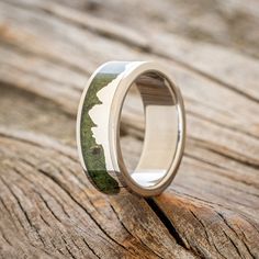 a wedding ring with a green and white camo print on the inside is sitting on a piece of wood