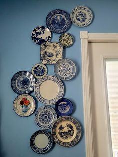 a bunch of plates are hanging on the wall next to a window in a room with blue walls