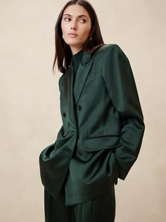 a woman in a dark green suit poses for the camera with her hands on her hips