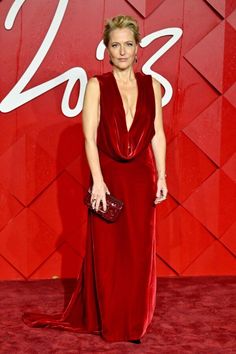 a woman in a red dress standing on a red carpet with her hands in her pockets