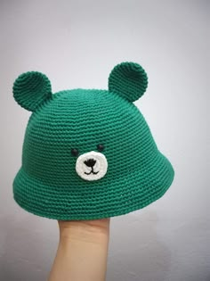 a hand holding up a green knitted hat with a bear's head on it